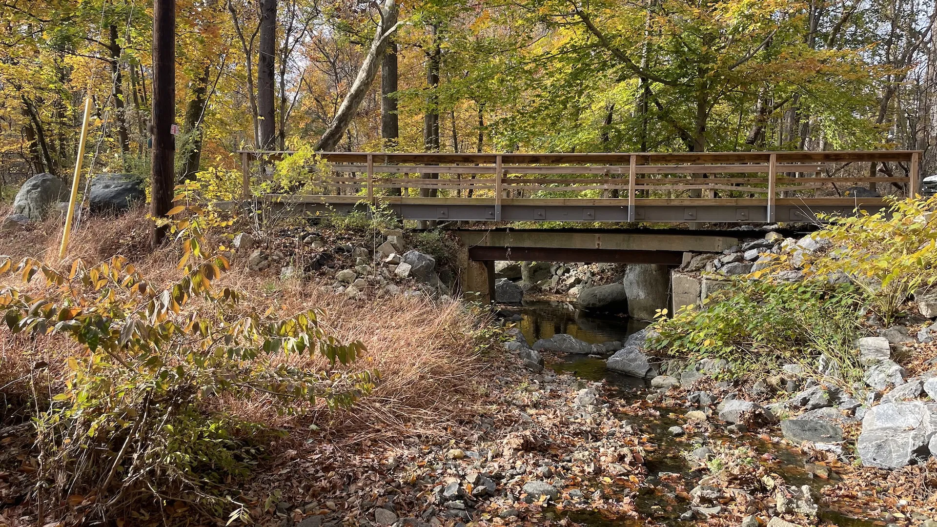 E&H timber bridge installed as an overlay on an existing structure over a rocky stream in a wooded Maryland setting